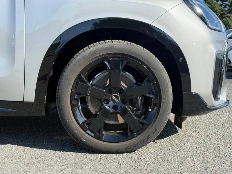 Gros plan sur la roue avant droite noire brillante d’un MINI Countryman argenté avec détails du frein visible.