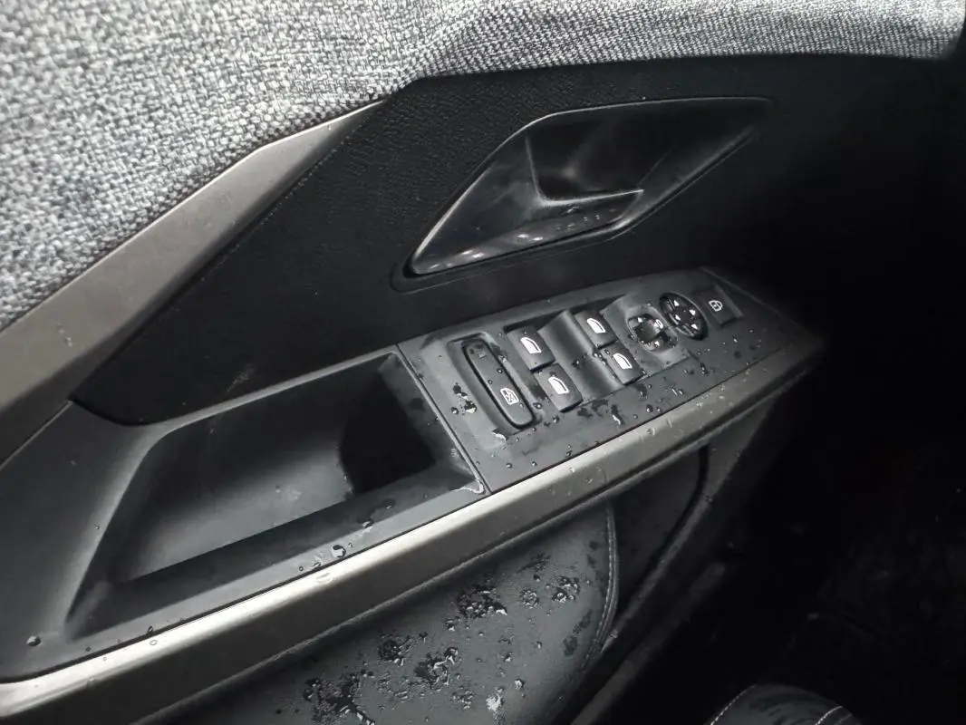 Gros plan sur la commande des vitres et rétroviseurs côté conducteur du Peugeot 3008 Hybrid noir, intérieur humide.