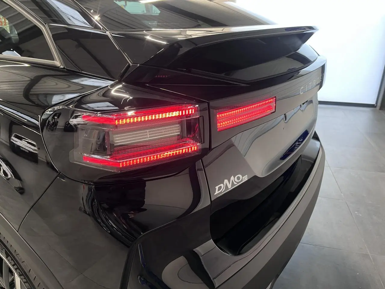 Vue arrière droite d'une Citroën C4 noire métal avec feux LED allumés et logo DMO visible sur le coffre.