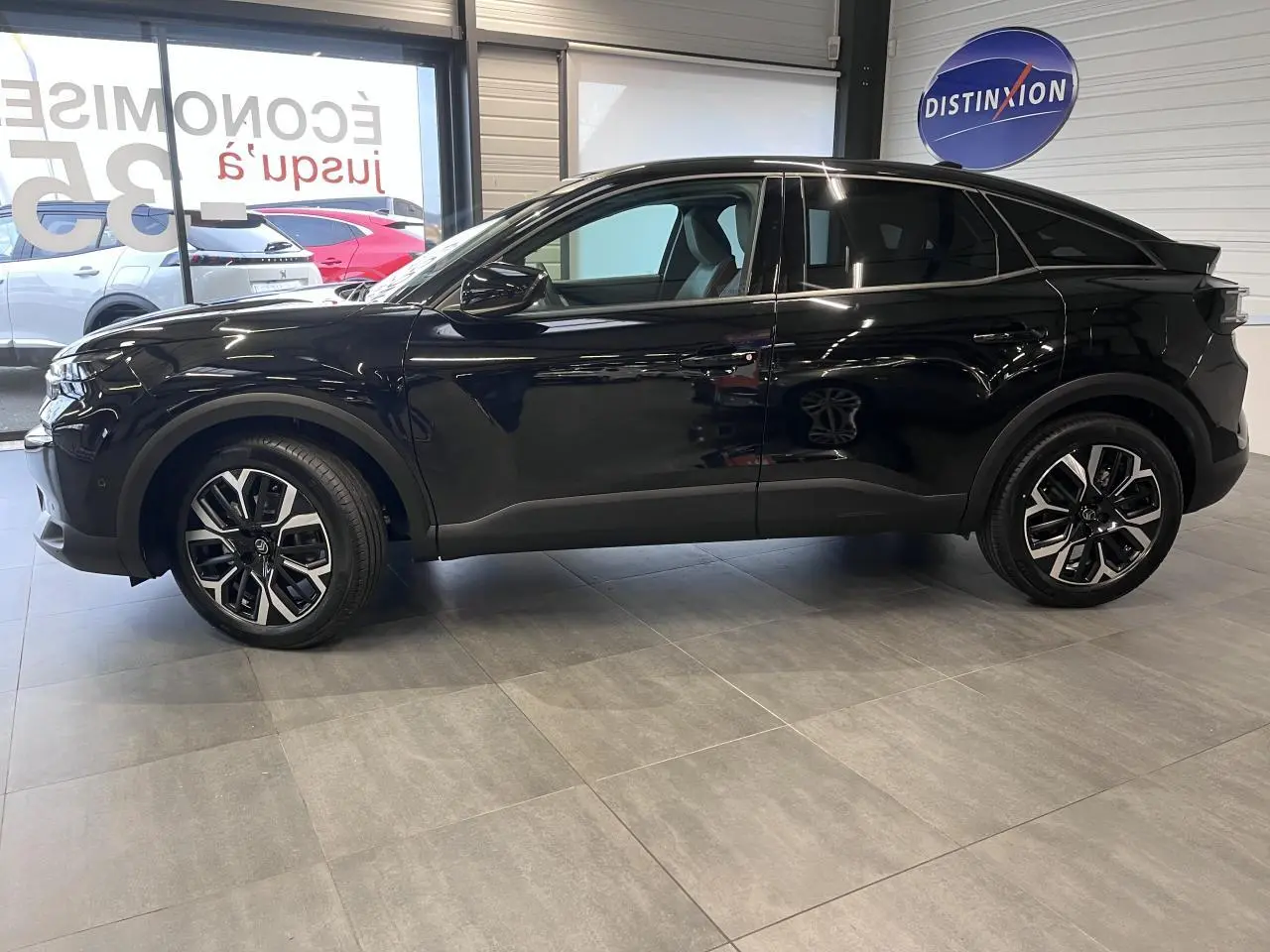 Vue latérale droite d'une Citroën C4 noire métal 2025 en showroom, avec jantes alliage 18 pouces et vitres surteintées.