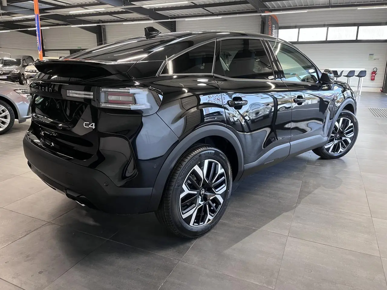 Vue 3/4 arrière droite d'une Citroën C4 noire métallisée avec jantes alliage 18'' et feux arrière LED en showroom.