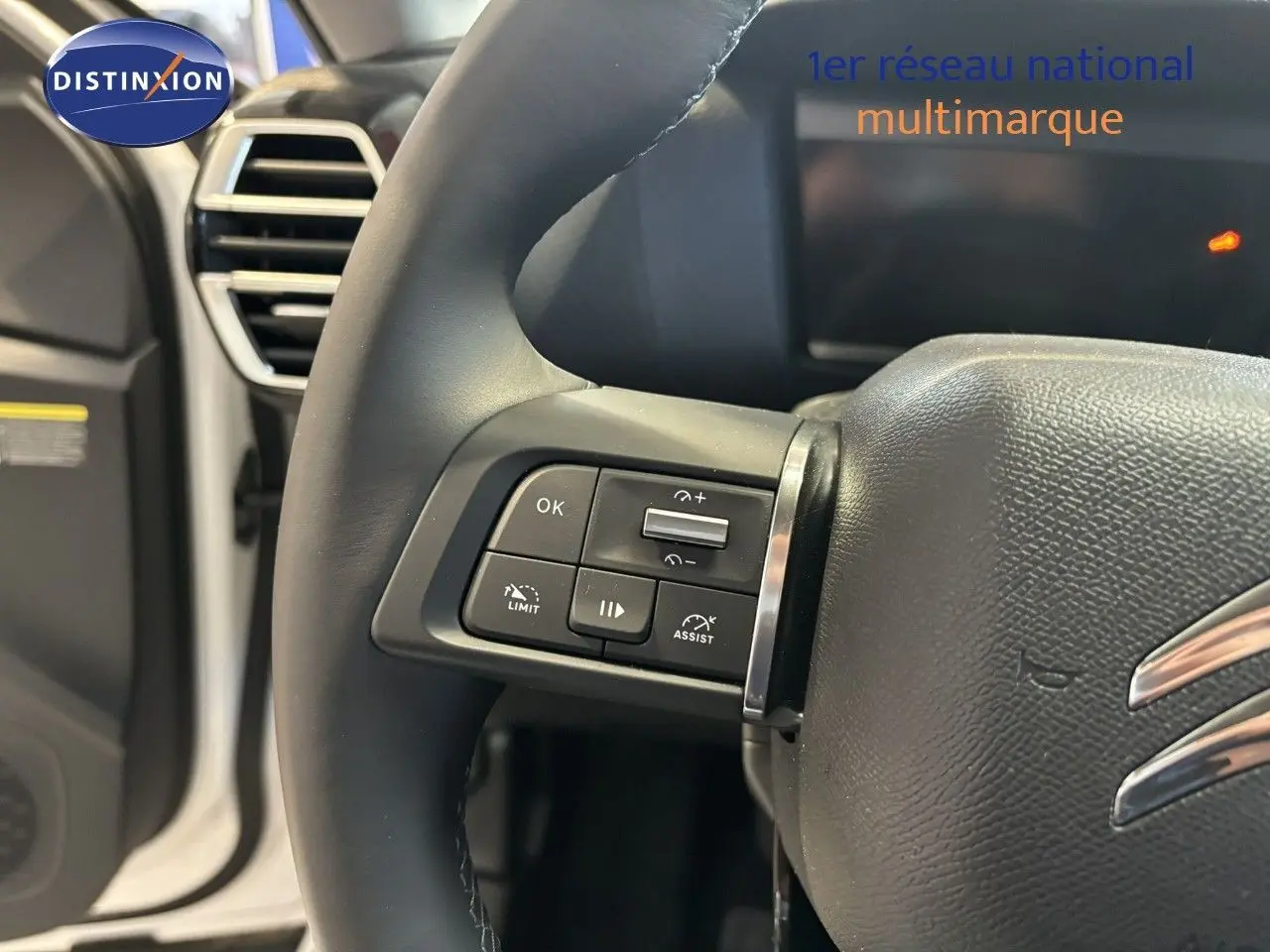 Gros plan sur le volant multifonction noir de la Citroën C4 blanche, mettant en valeur les commandes de régulateur et limiteur de vitesse.