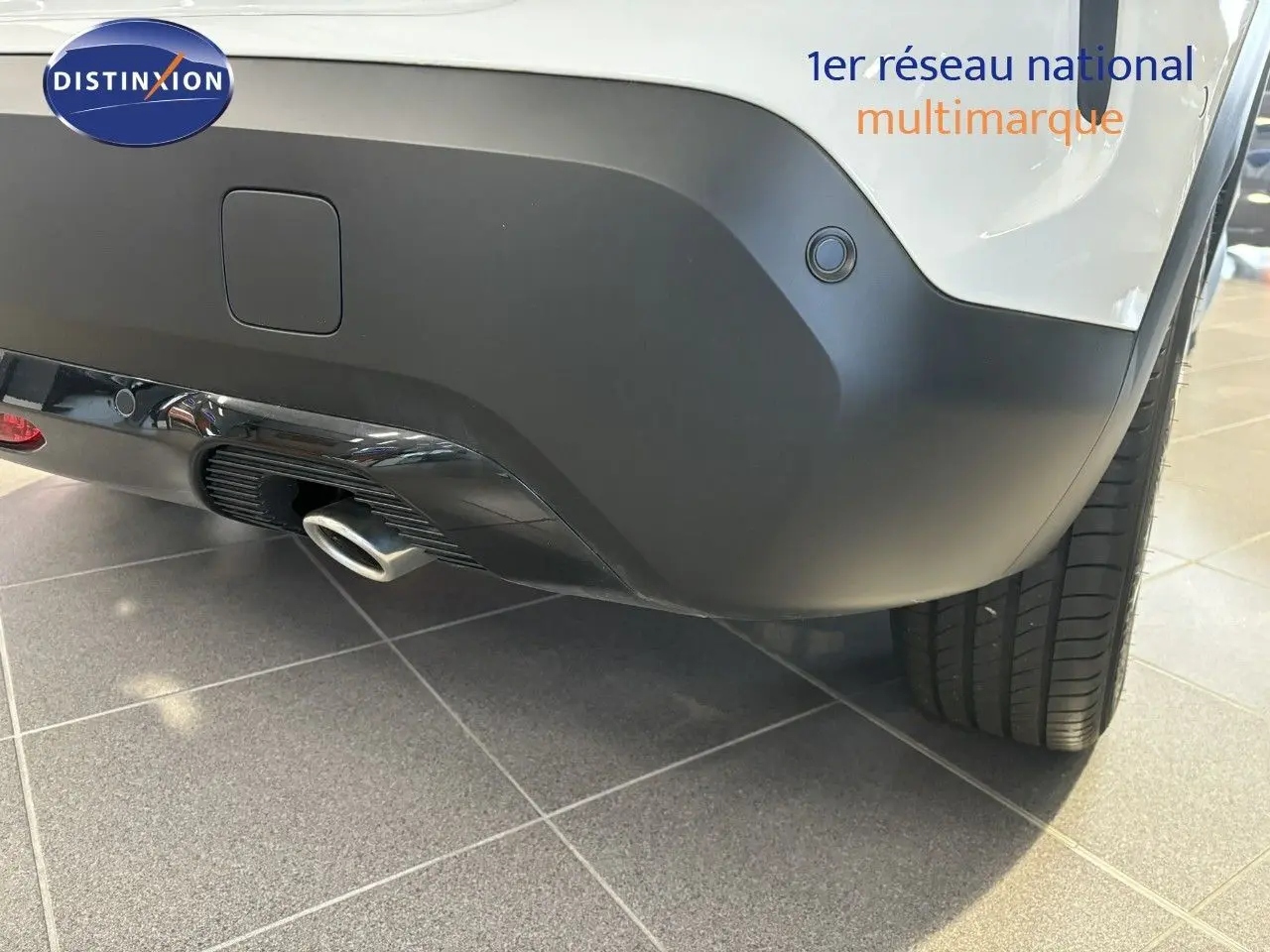 Gros plan sur le pare-chocs arrière droit blanc d'une Citroën C4 2022 avec sortie d'échappement et capteur de recul.