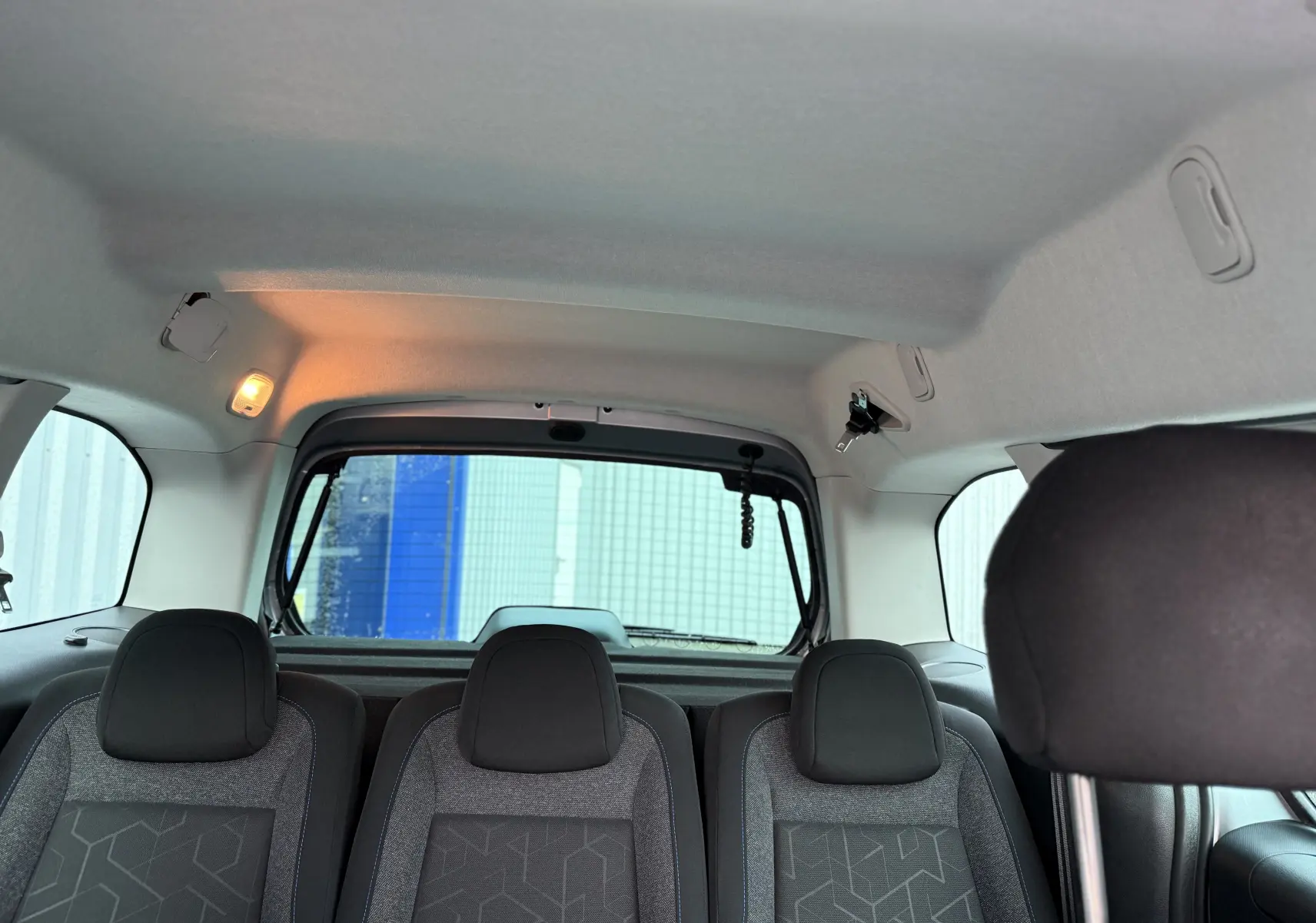 Vue intérieure arrière du Peugeot Partner Tepee gris 2018, montrant les sièges tissu et la lunette arrière.