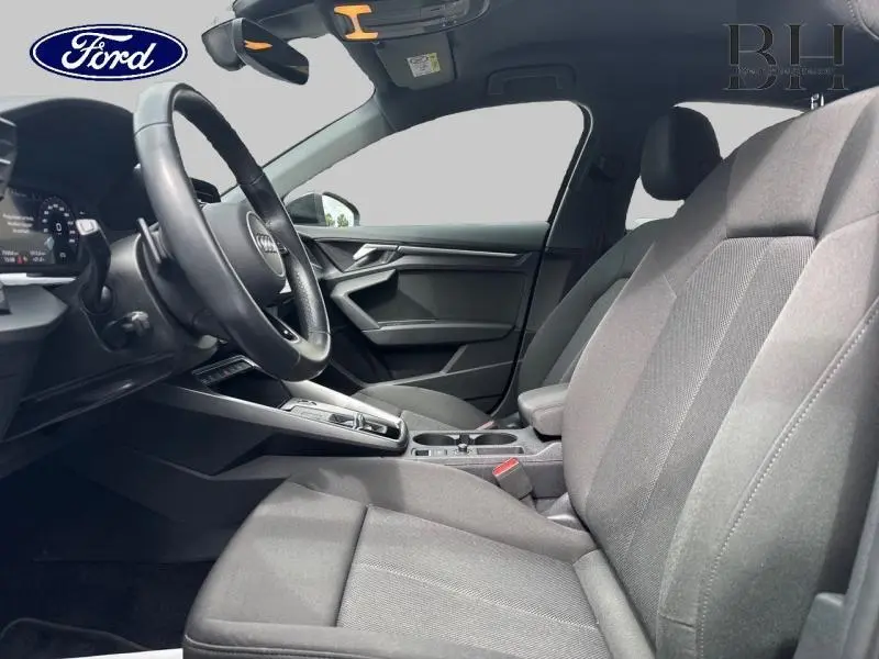 Vue intérieure côté conducteur de l'Audi A3 Sportback 35 TDI 2022 avec sièges tissu noir et volant cuir multifonction.