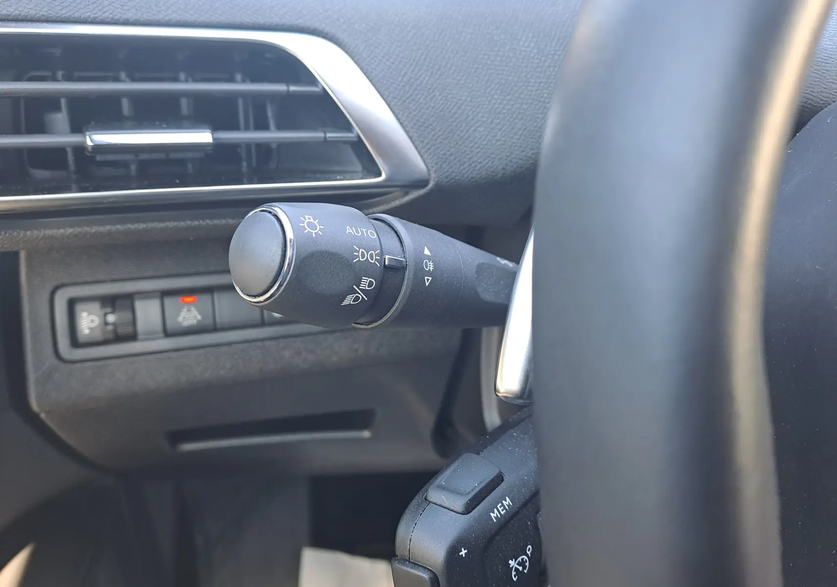Gros plan sur la commande des phares à gauche du volant dans l’habitacle noir du Peugeot 3008 blanc nacré 2023.