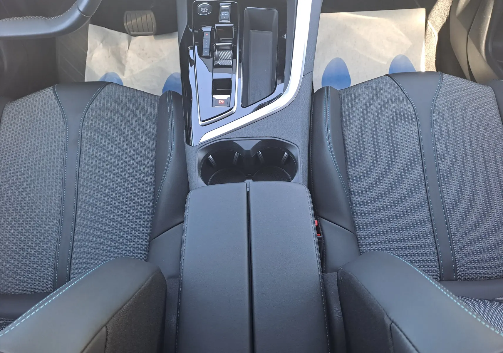 Vue intérieure plongeante sur la console centrale noire et les sièges avant en tissu gris du Peugeot 3008 2023.