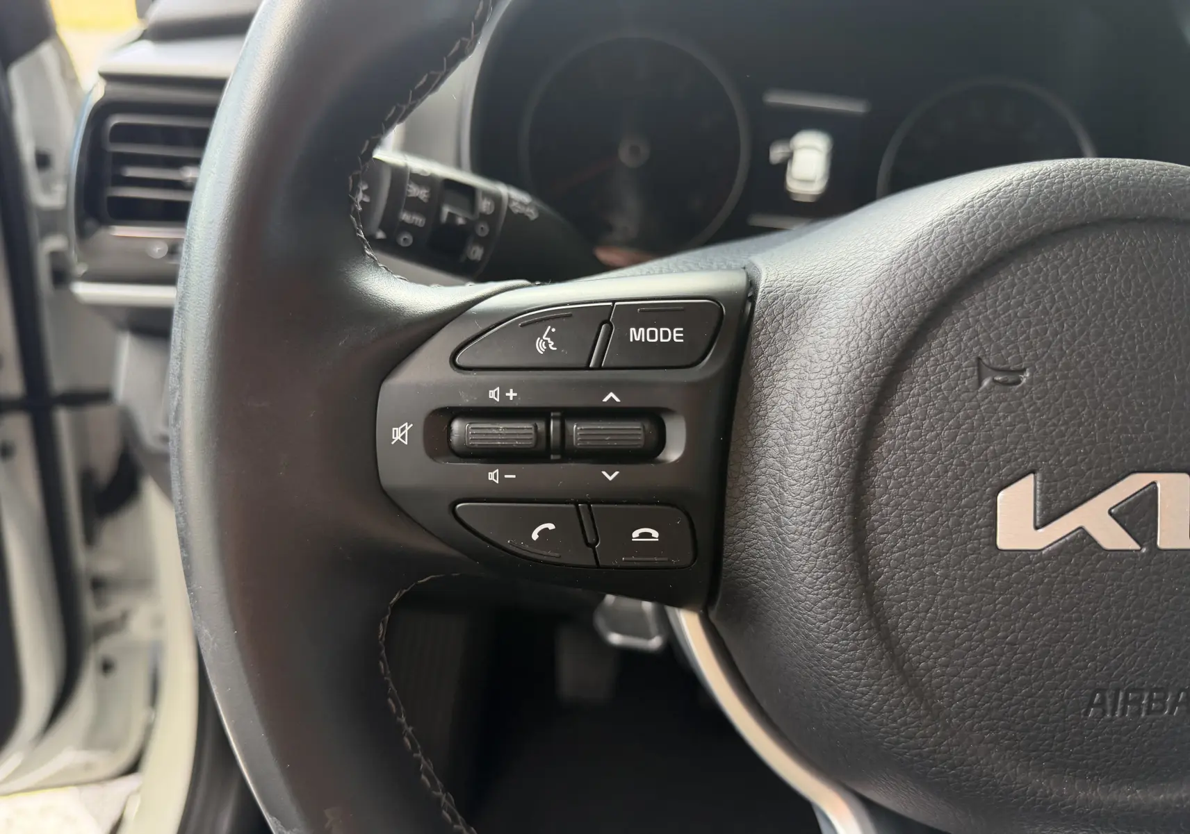 Gros plan sur le volant côté gauche du KIA STONIC blanc 2023, montrant les commandes audio et téléphone intégrées.