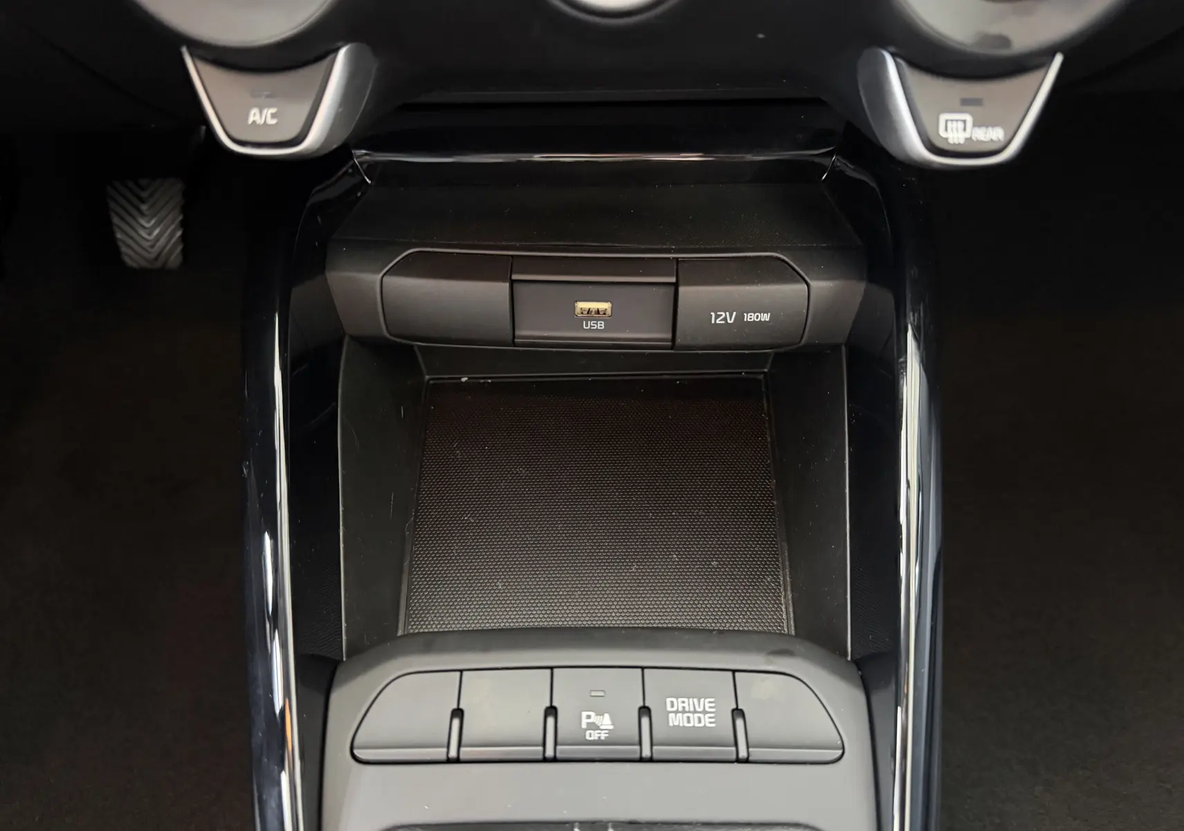 Vue rapprochée de la console centrale noire du Kia Stonic 2023, avec ports USB et 12V, boutons de mode de conduite et assistance parking.