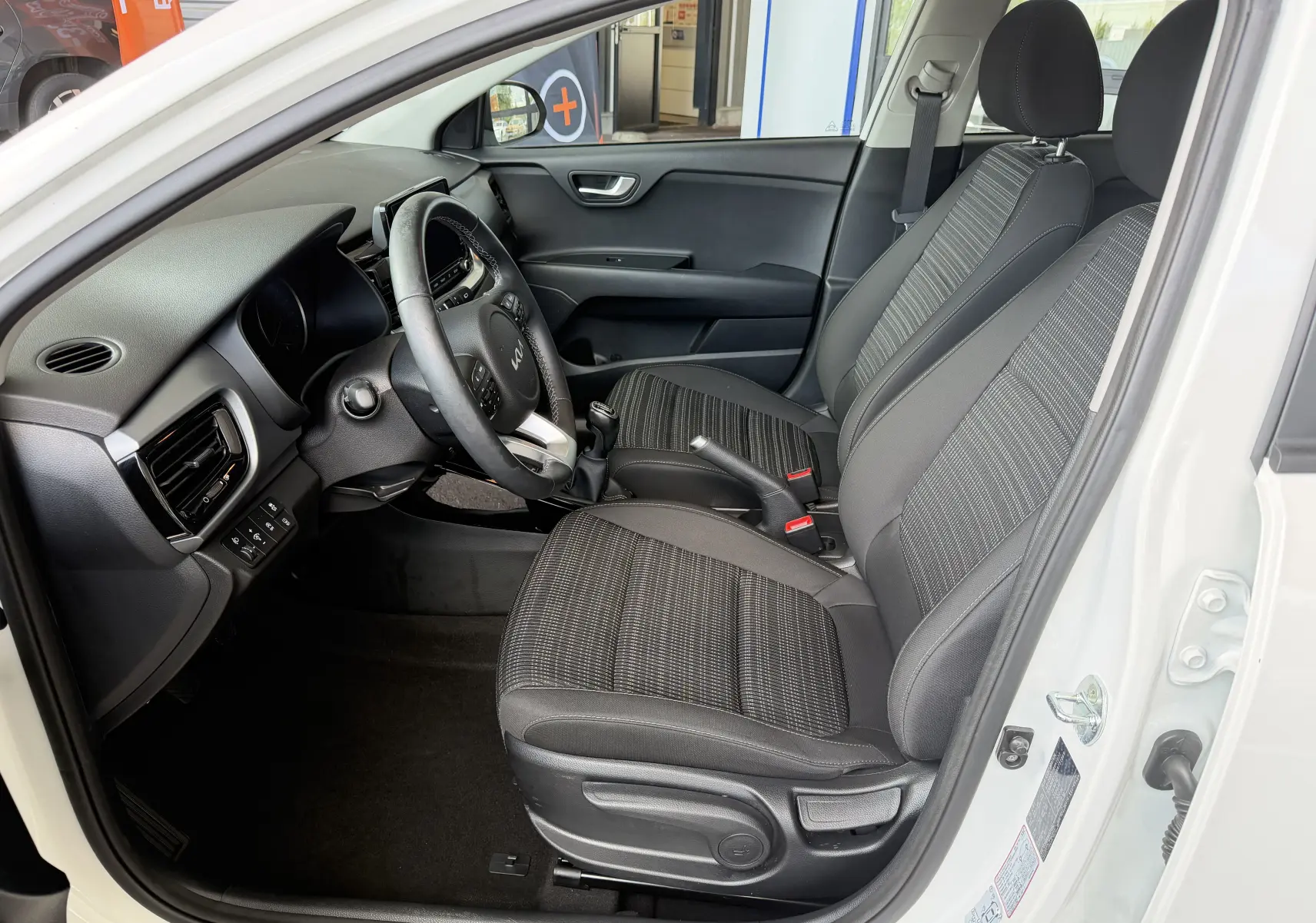 Intérieur de la KIA STONIC blanc, vue côté conducteur, montrant les sièges noirs et le volant multifonction.