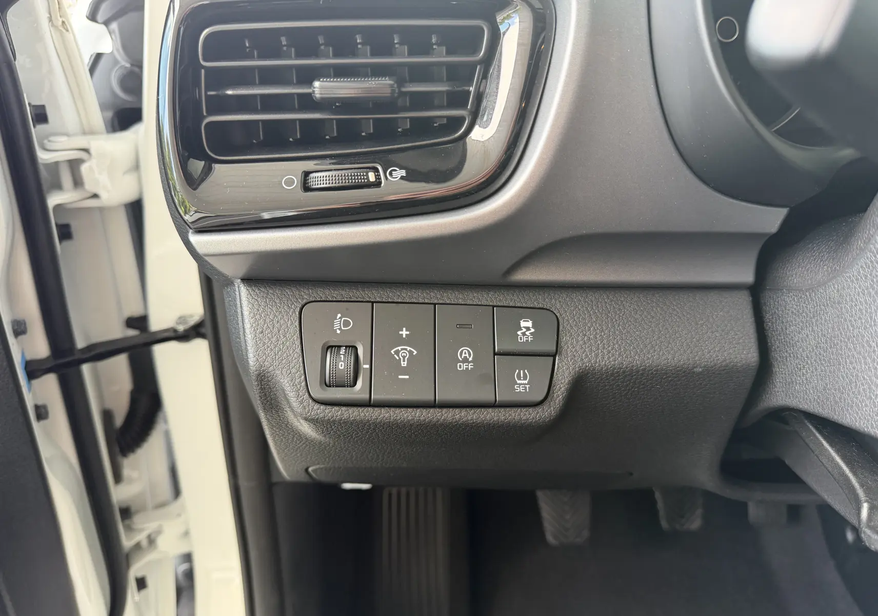Détail intérieur côté gauche du tableau de bord blanc du Kia Stonic 2023 avec commandes d’éclairage et sécurité.