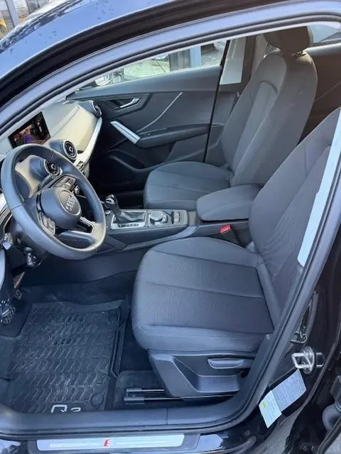 Vue intérieure côté conducteur de l'Audi Q2 noir 2023, sièges tissu gris, volant cuir multifonctions et console centrale visible.