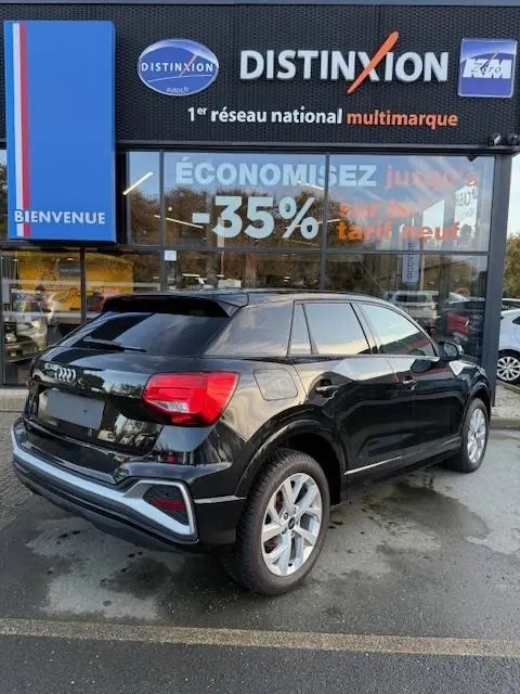 Audi Q2 35 TFSI S Line noir vue 3/4 arrière droit, stationné devant une concession multimarque Distinxion.