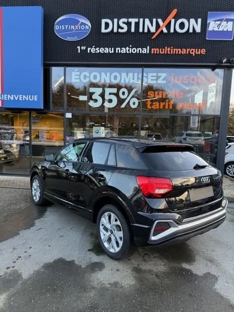 Audi Q2 35 TFSI S Line noir vue 3/4 arrière droit, stationné devant un showroom Distinxion.