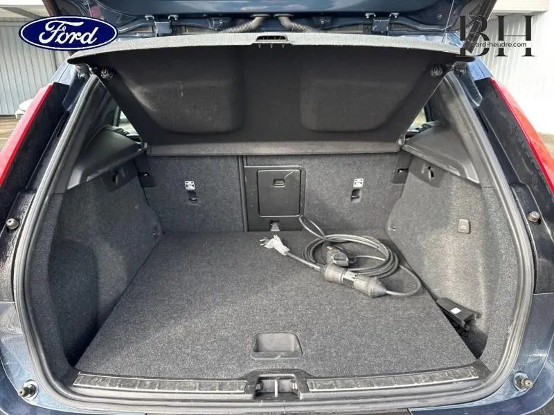 Coffre ouvert vu de l'arrière d'un Volvo XC40 Bleu Denim avec câble de recharge hybride visible.