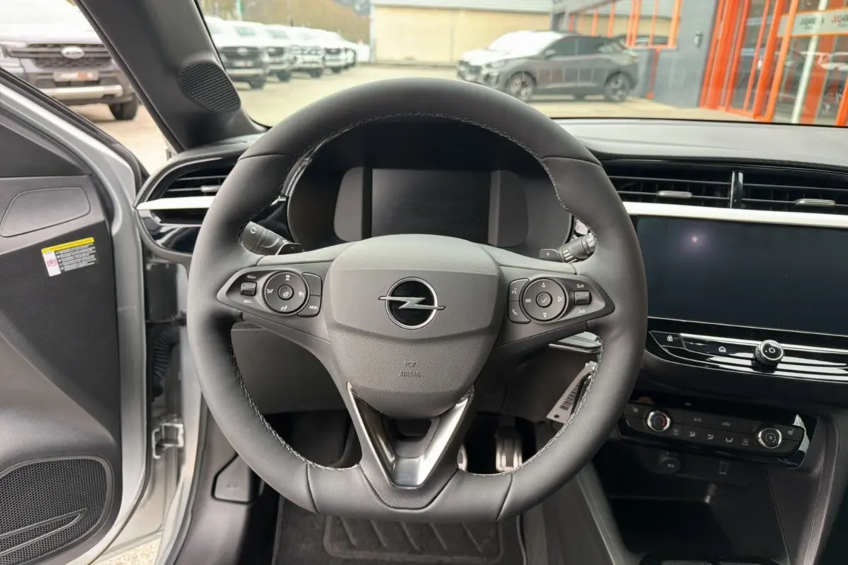 Vue intérieure centrée sur le volant cuir multifonctions d’une Opel Corsa gris kristall avec tableau de bord moderne.