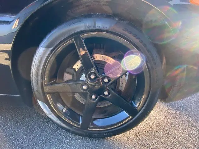 Gros plan sur la jante noire à cinq branches de la Chevrolet Corvette C6 Targa 2005 avec disque de frein perforé visible.