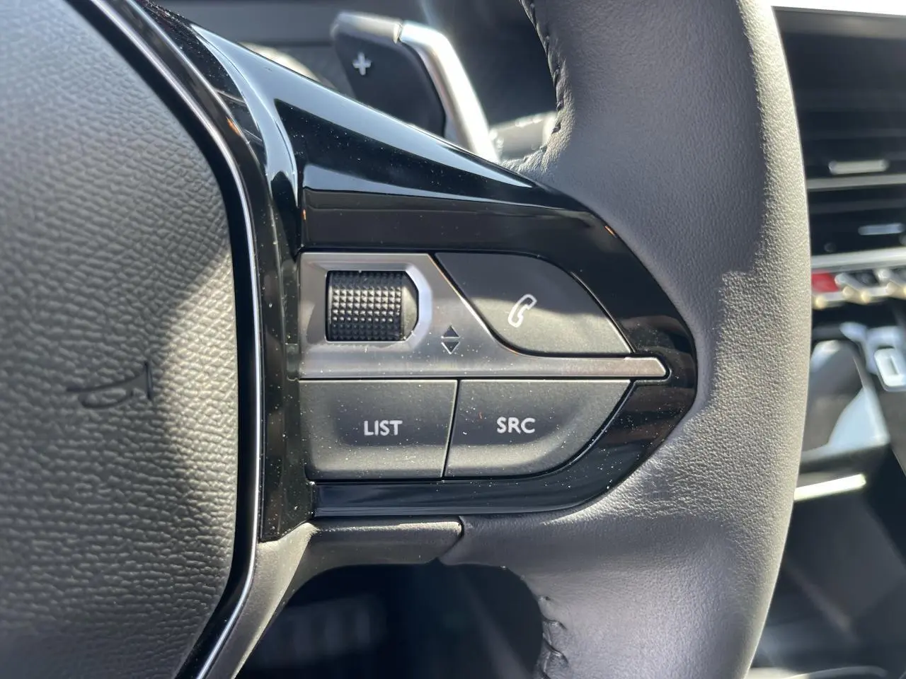 Gros plan sur les commandes gauche du volant cuir noir du Peugeot 208 New II 2024, avec boutons multifonctions.