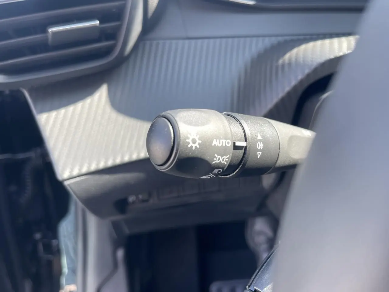 Gros plan sur la commande des feux automatique dans l'habitacle noir du Peugeot 208 New II 2024.