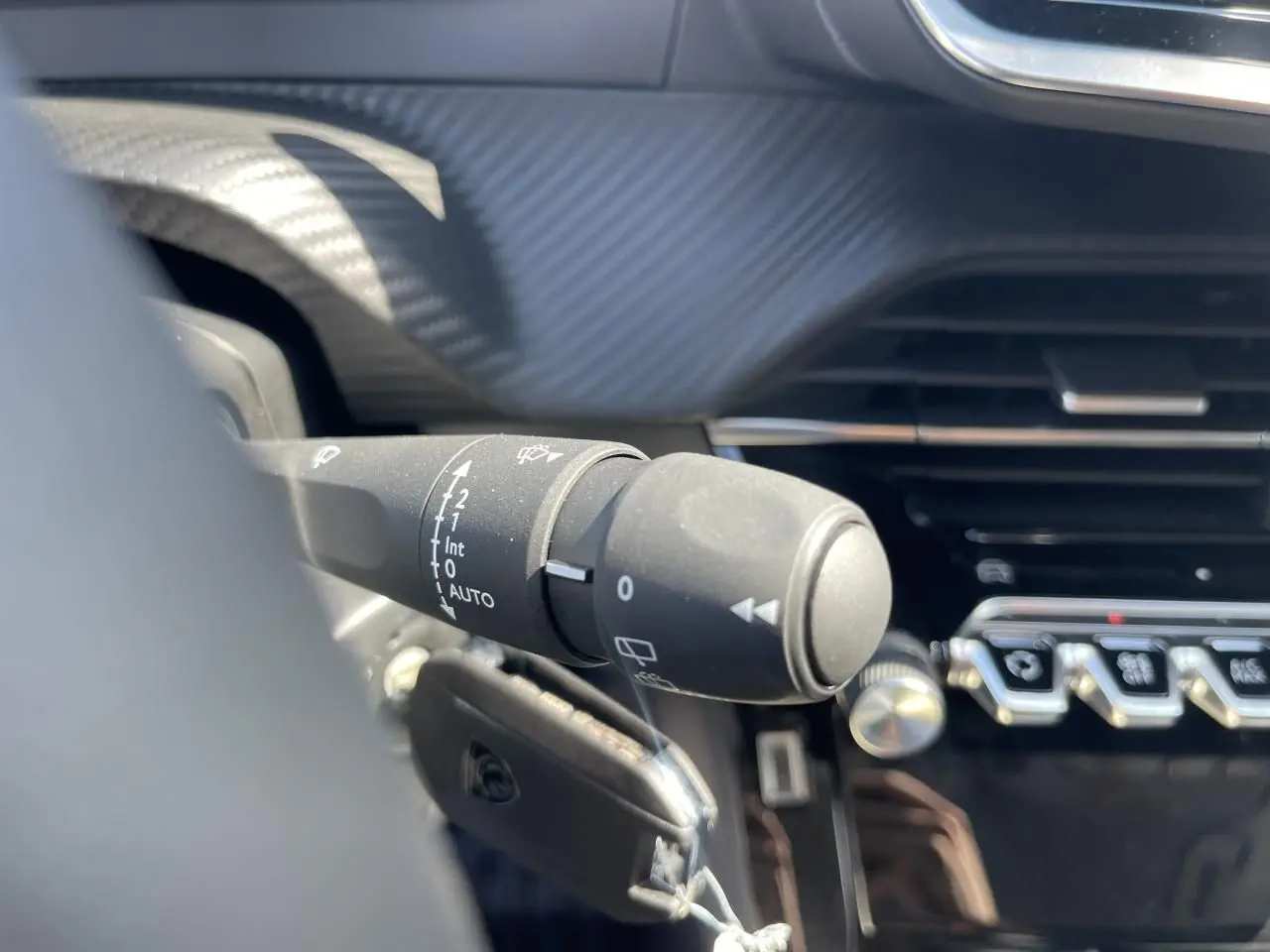 Gros plan sur la commande d'essuie-glace à gauche du volant dans l'habitacle noir du Peugeot 208 2024.
