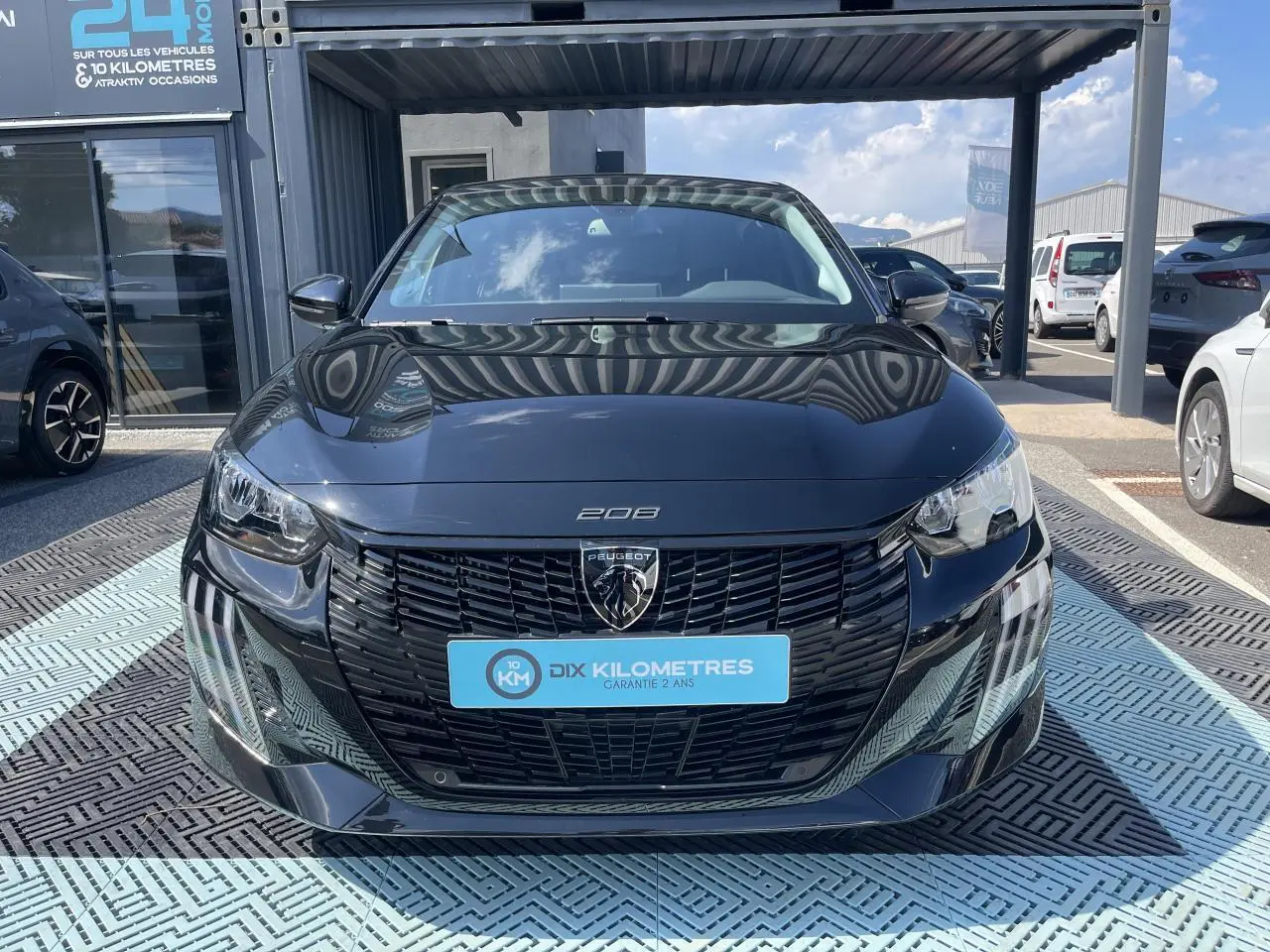 Vue frontale d'une Peugeot 208 noire Onyx avec calandre noire et feux LED 3 griffes, stationnée en extérieur.
