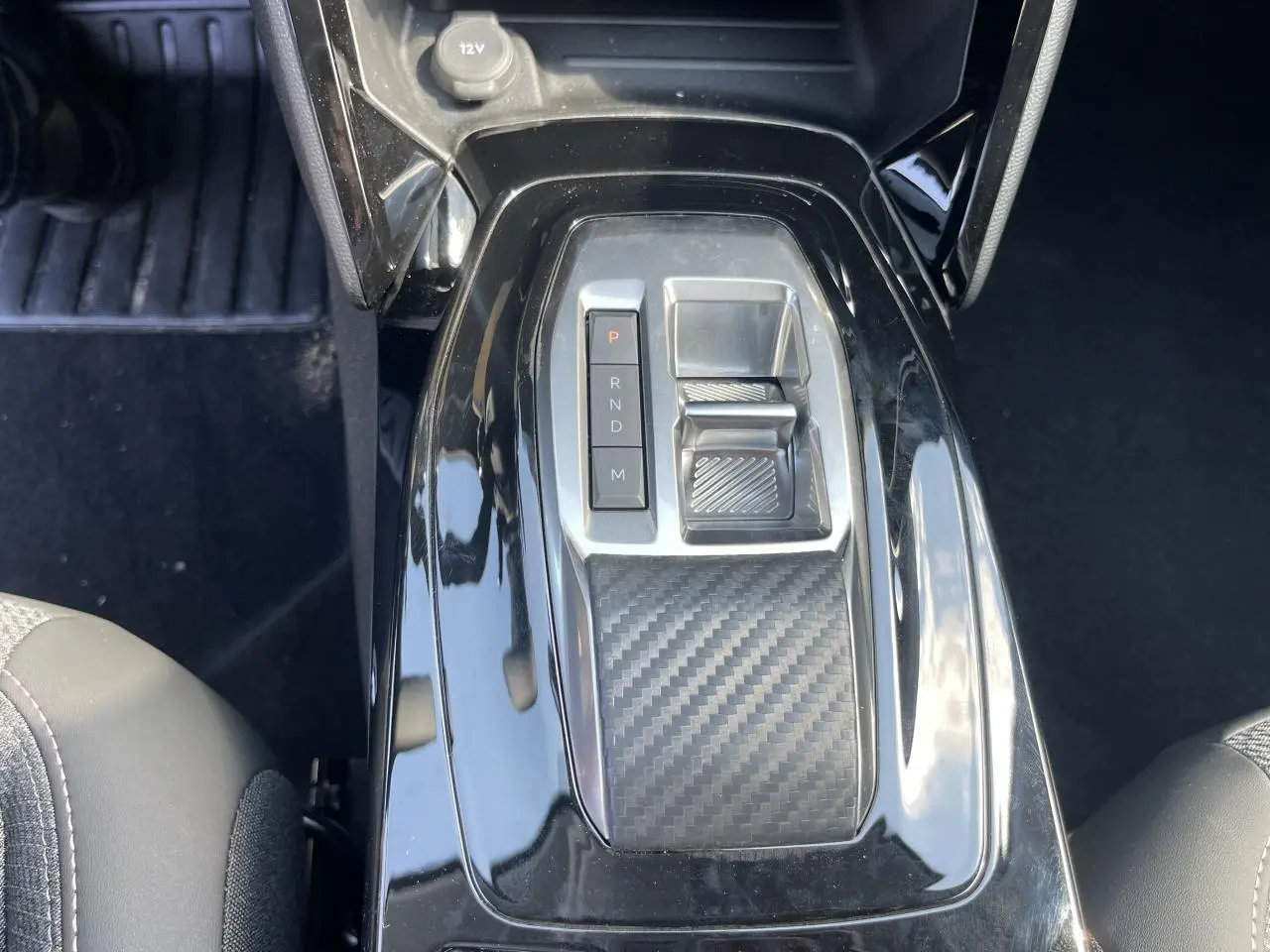 Vue rapprochée de la console centrale noire brillante avec sélecteur de boîte auto et surface effet carbone sur Peugeot 208 2024.