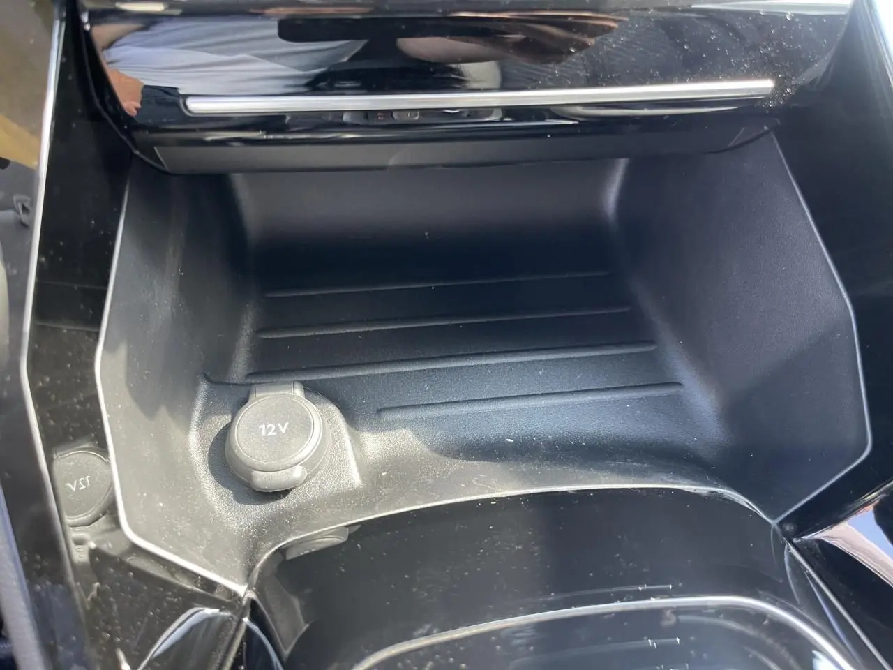Prise 12V dans la console centrale noire brillante d'une Peugeot 208 noir Onyx, version 2024 vue en gros plan.