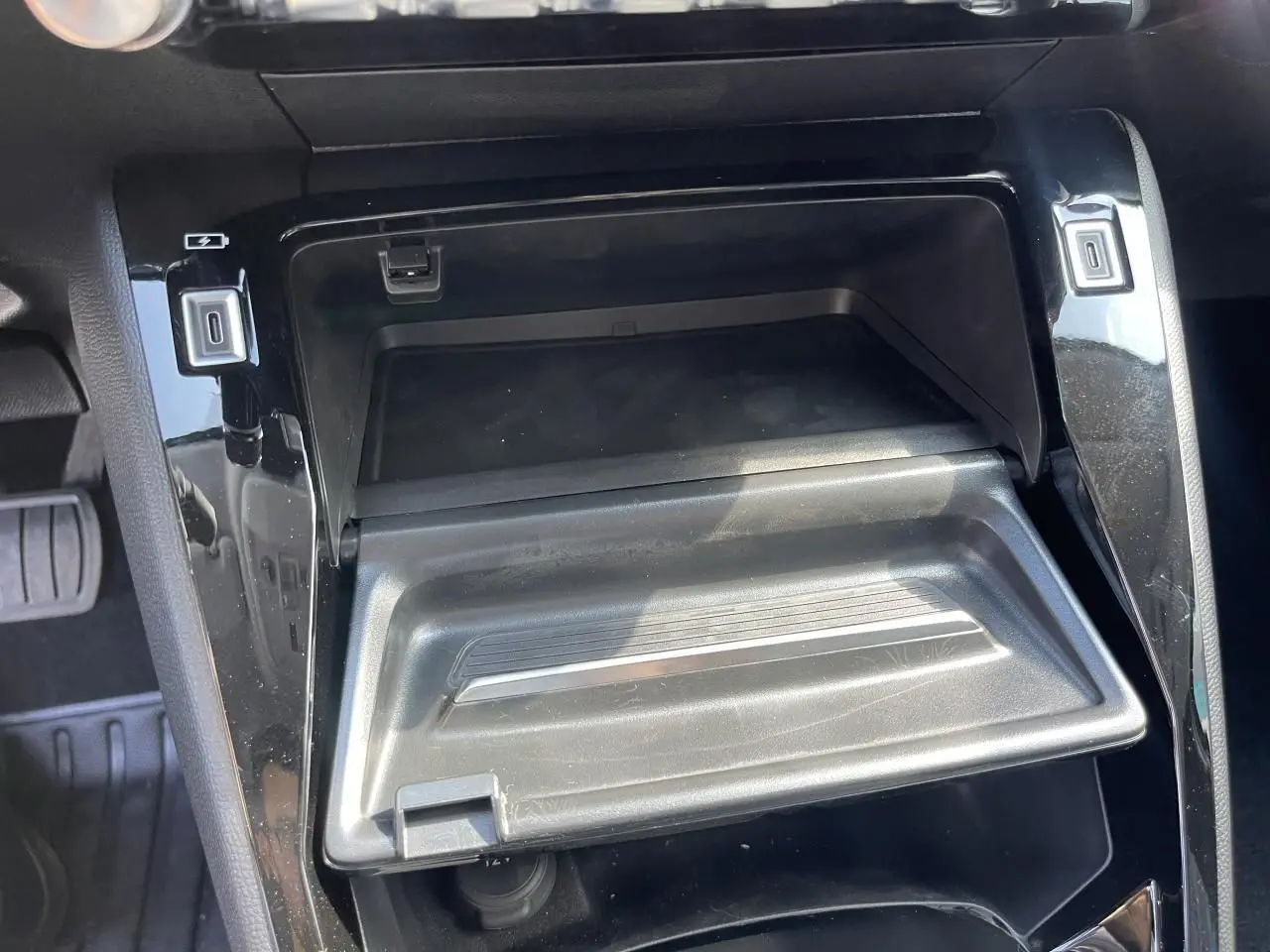 Gros plan sur la console centrale noire brillante de la Peugeot 208 2024 avec compartiment ouvert et prises USB visibles.