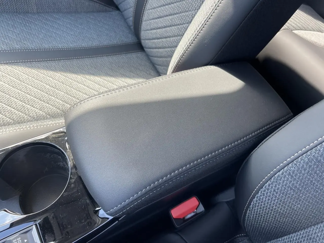 Gros plan sur l'accoudoir central noir et la sellerie tissu gris du PEUGEOT 208 NEW II 2024 côté console centrale.