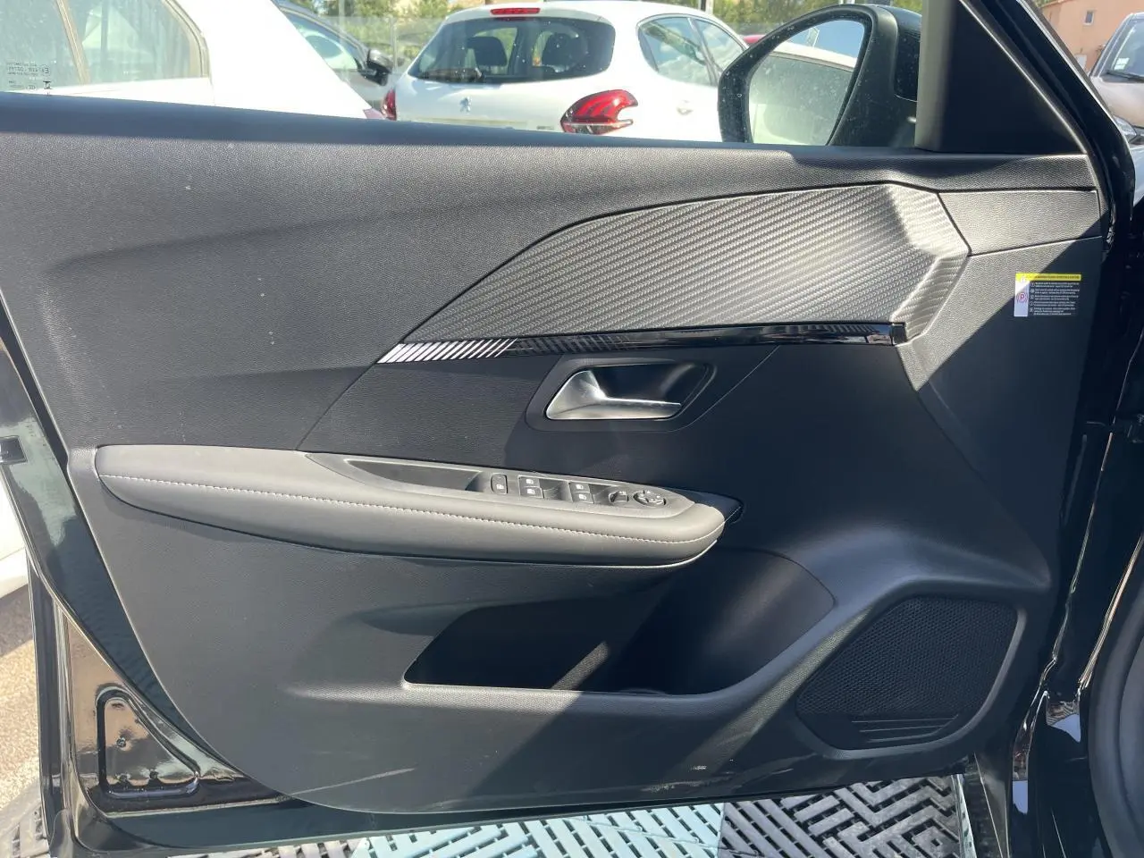 Porte avant gauche ouverte d'une Peugeot 208 noire Onyx, montrant les commandes électriques et le design texturé intérieur.