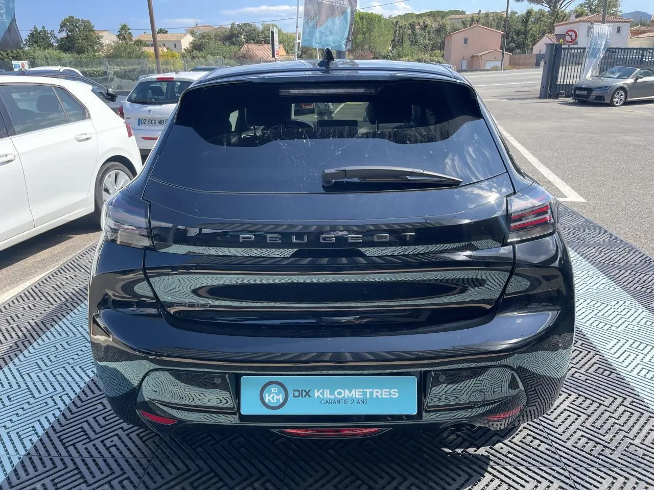 Vue arrière d'une Peugeot 208 noire Onyx 2024 avec feux LED 3 griffes et logo Peugeot lumineux sur le hayon.
