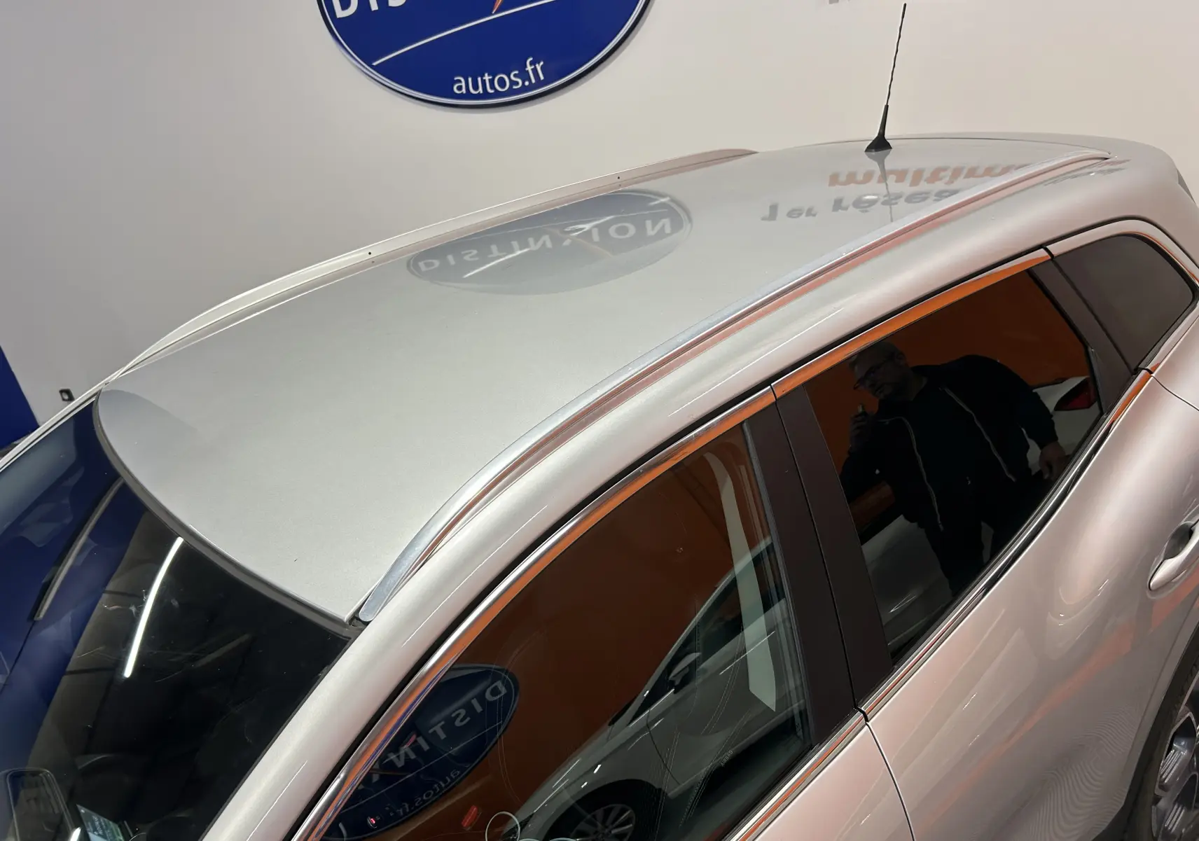 Vue en plongée du côté gauche d'un Renault Kadjar gris métallisé, avec toit et vitres teintées visibles en intérieur showroom.