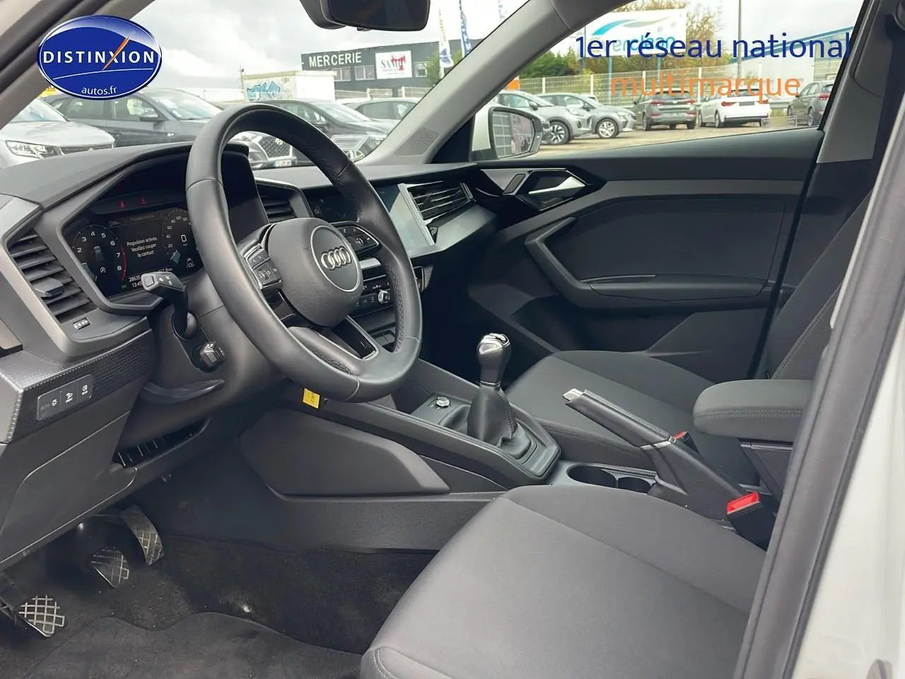 Intérieur de l'Audi A1 Sportback blanc 2022 vu côté conducteur, volant cuir sport et boîte manuelle visibles.