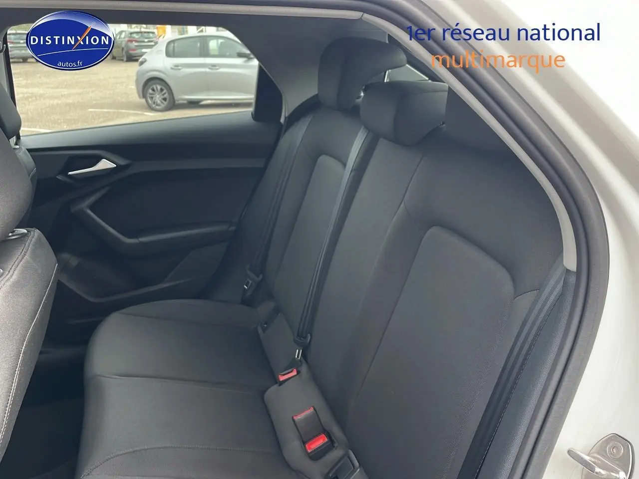 Vue intérieure sur la banquette arrière noire de l'Audi A1 Sportback blanche, côté droit avec appuie-tête et ceintures visibles.