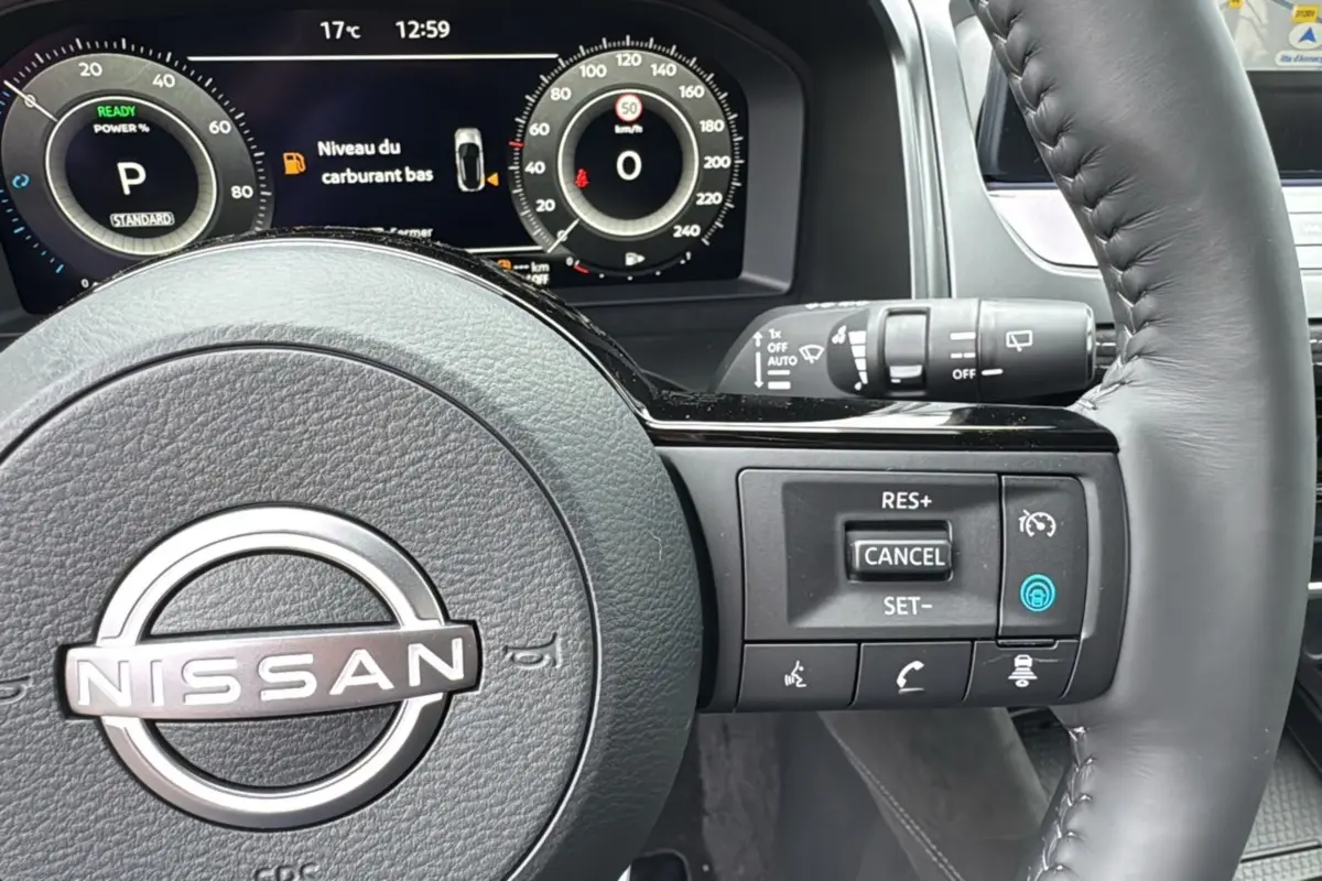 Gros plan sur le volant cuir multifonctions d’un Nissan Qashqai E-POWER 205 Tekna Plus avec affichage numérique du tableau de bord.