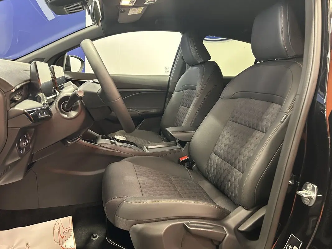 Vue intérieure côté conducteur de la MG3 1.5 HYBRID+ 195 LUXURY 2026, sièges noirs cuir et tissu avec surpiqûres contrastées.