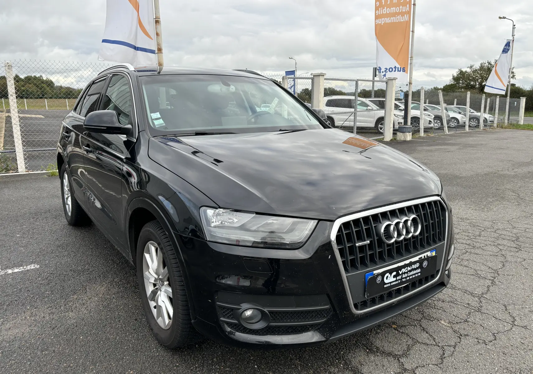 Audi Q3 noir vue 3/4 avant droit sur parking, calandre chromée et phares LED distinctifs visibles.