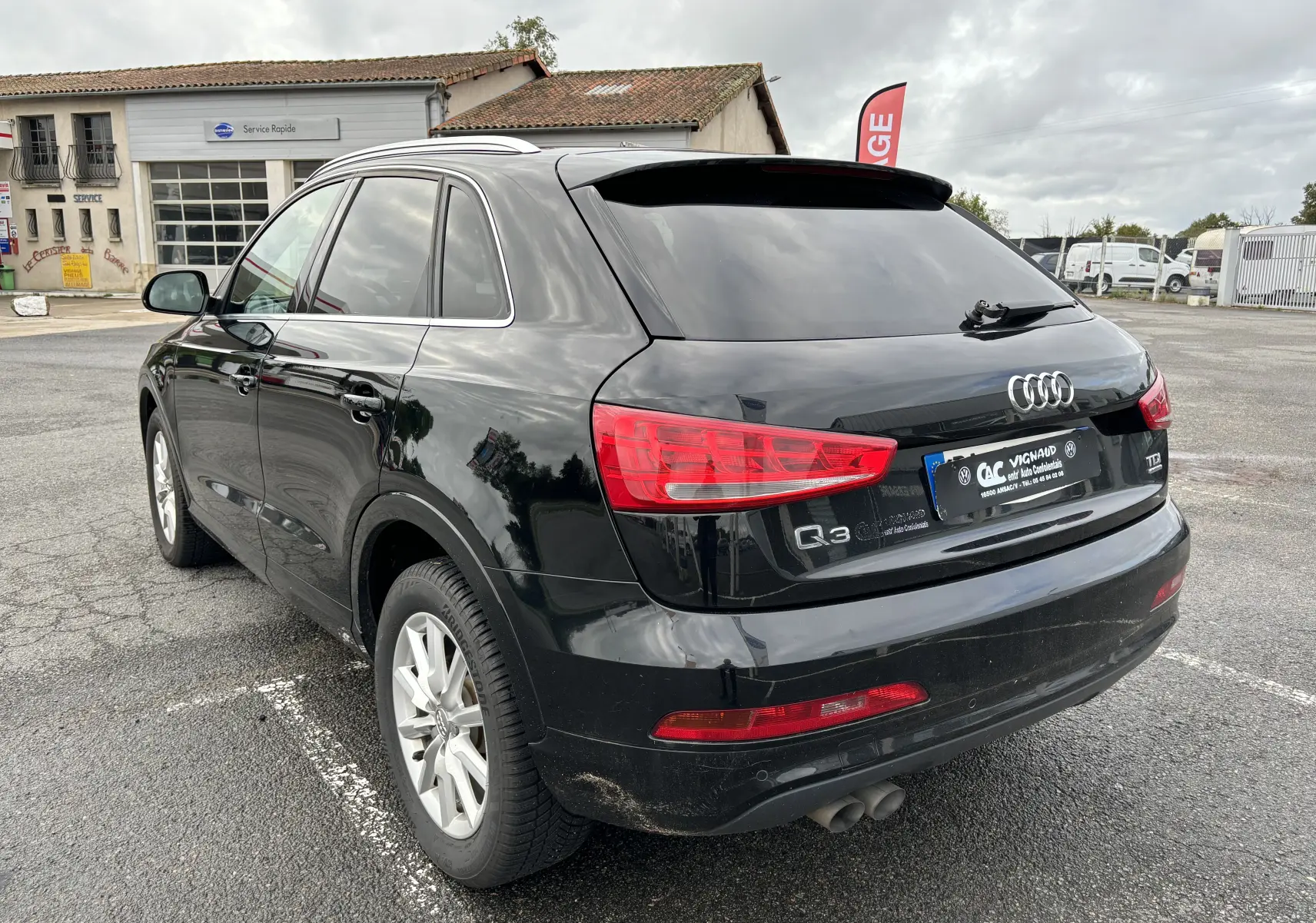 Audi Q3 noir vue 3/4 arrière droit, avec feux rouges et jantes argentées, stationné sur un parking extérieur.