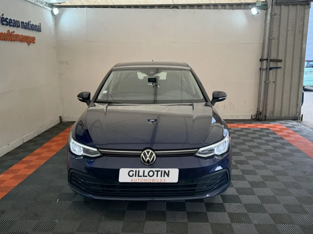 Vue frontale d'une Volkswagen Golf bleu foncé garée dans un garage avec plaque GILLOTIN visible.