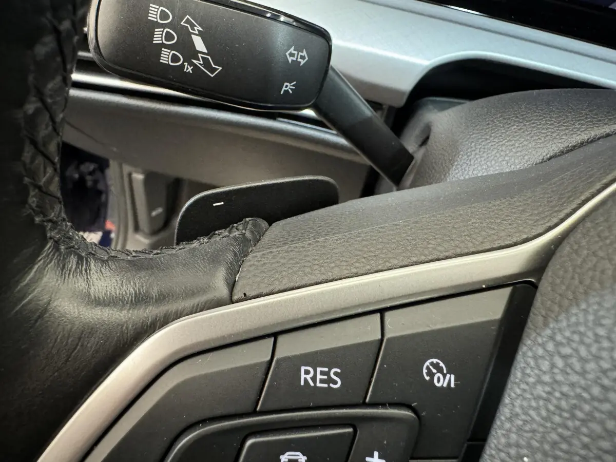 Gros plan sur les commandes au volant cuir noir de la Volkswagen Golf bleue, avec bouton régulateur de vitesse visible.