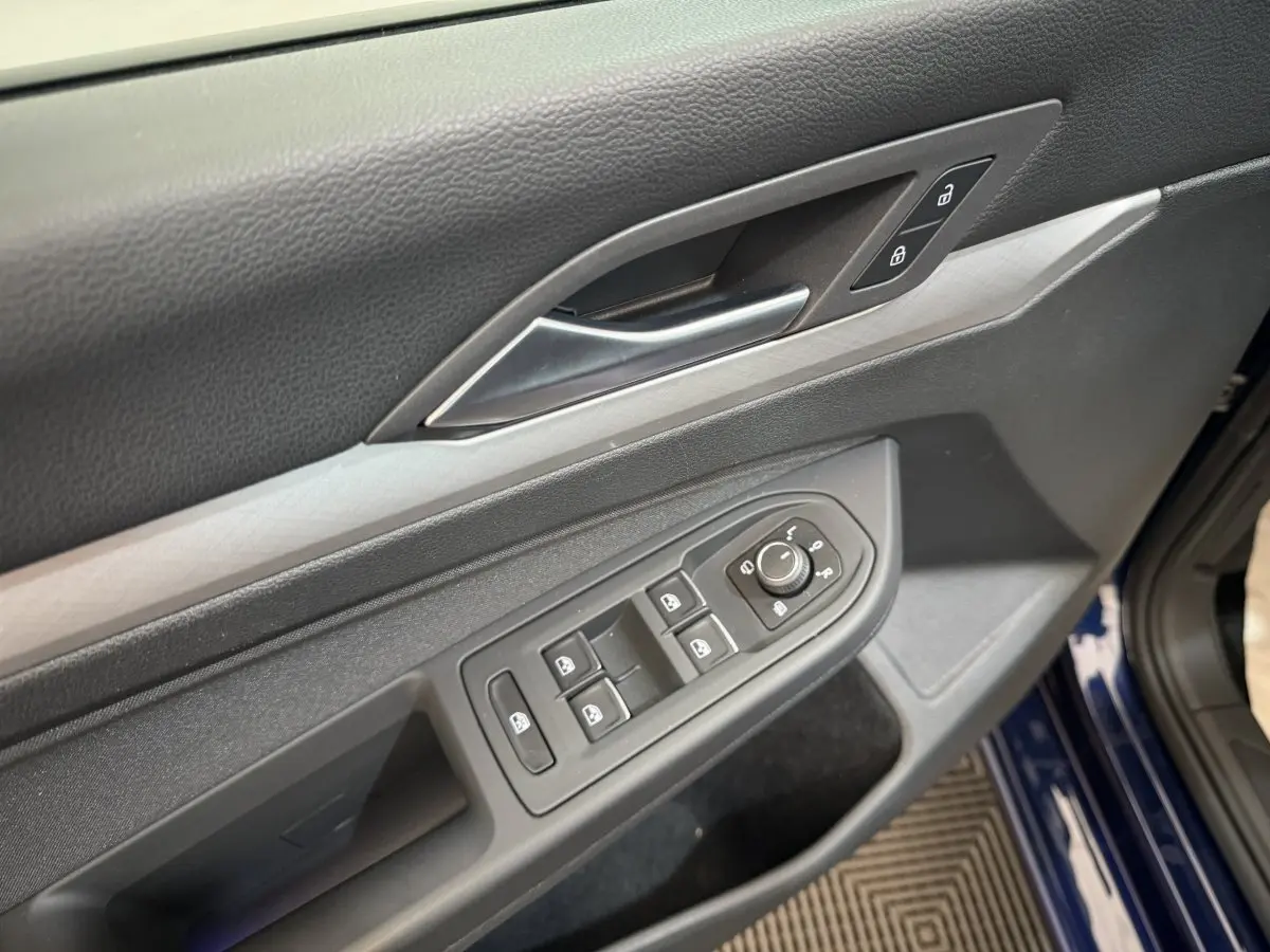 Gros plan sur la porte côté conducteur d’une Volkswagen Golf bleu 2021, avec commandes électriques et verrouillage.