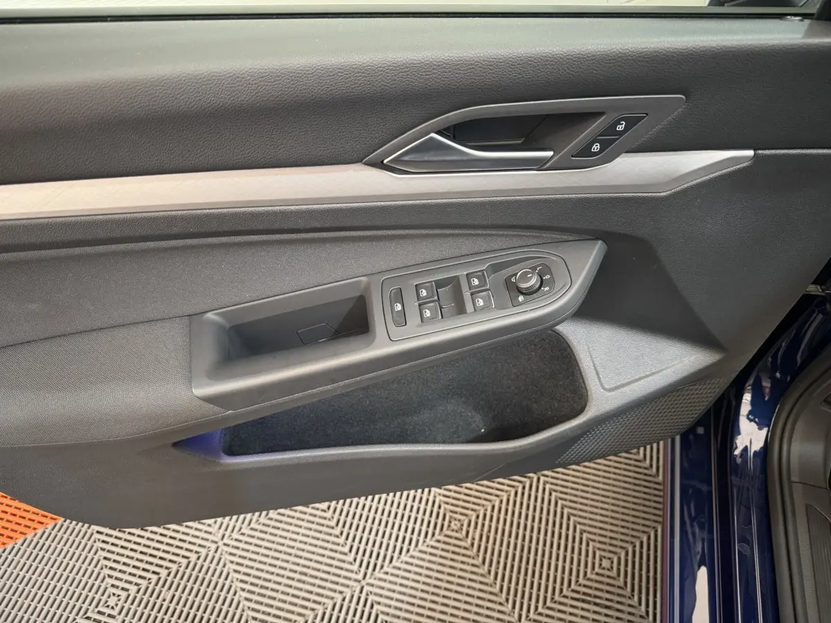 Vue rapprochée de la porte avant gauche d'une Volkswagen Golf bleu 2021, avec commandes de vitres et verrouillage.