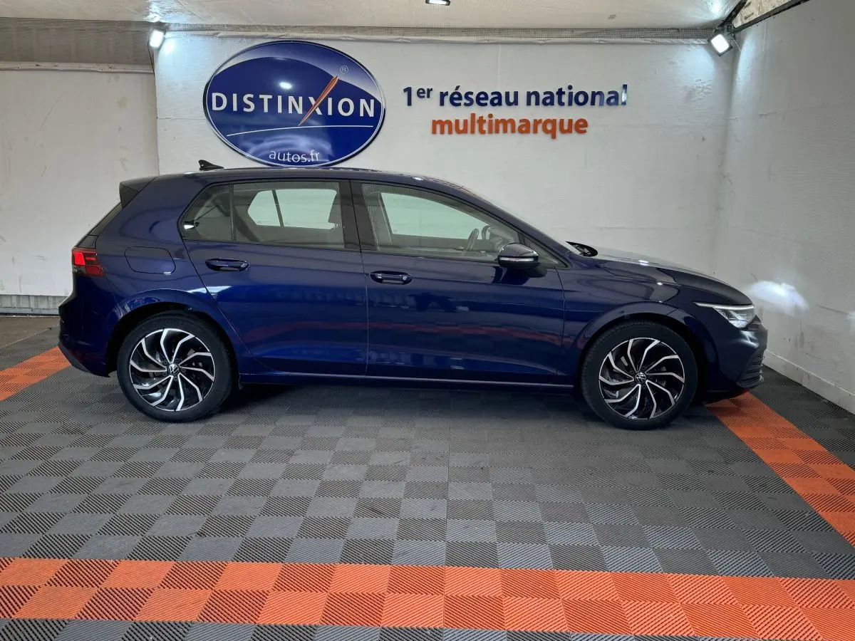 Profil côté gauche d'une Volkswagen Golf 2.0 TDI bleu foncé dans un showroom avec sol à damier gris et orange.