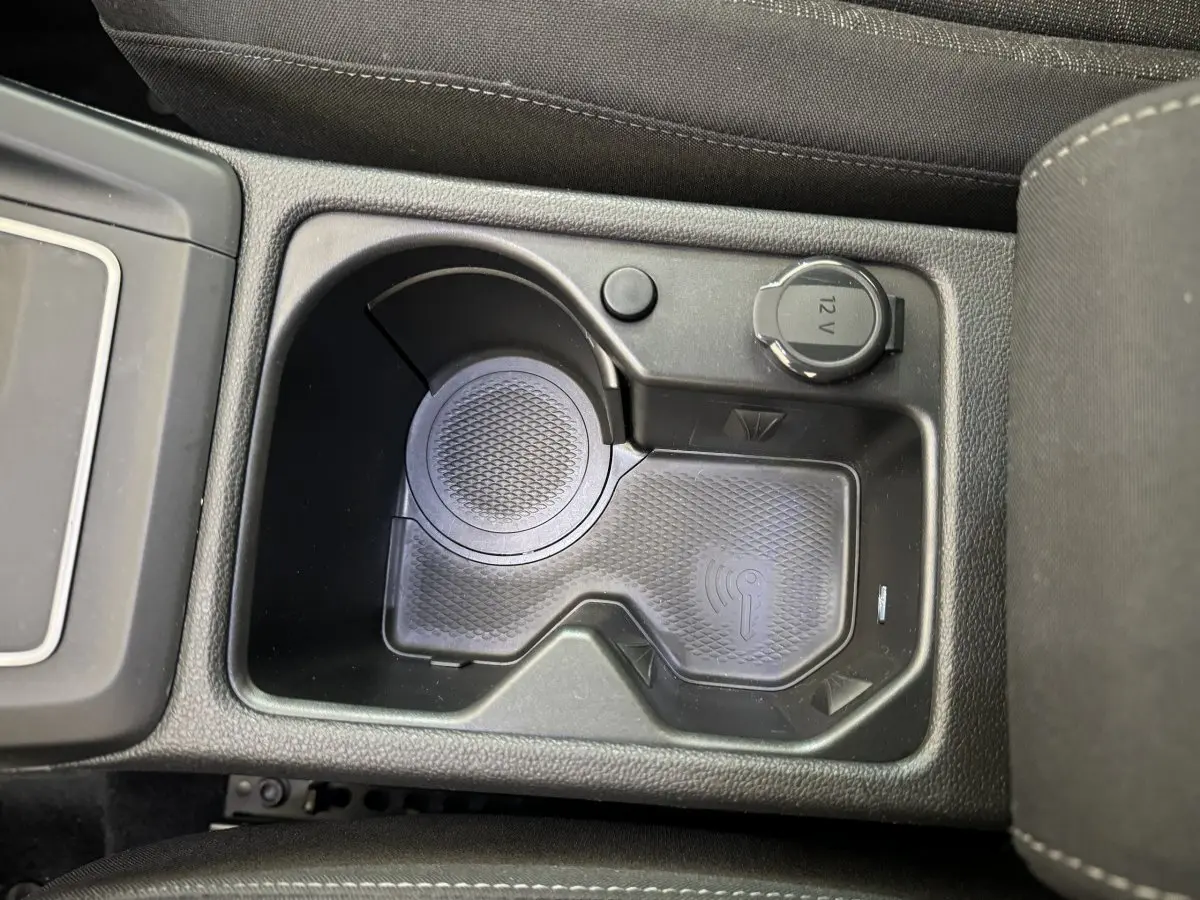Gros plan sur la console centrale noire de la Volkswagen Golf bleu, montrant un espace de recharge sans fil et une prise 12V.