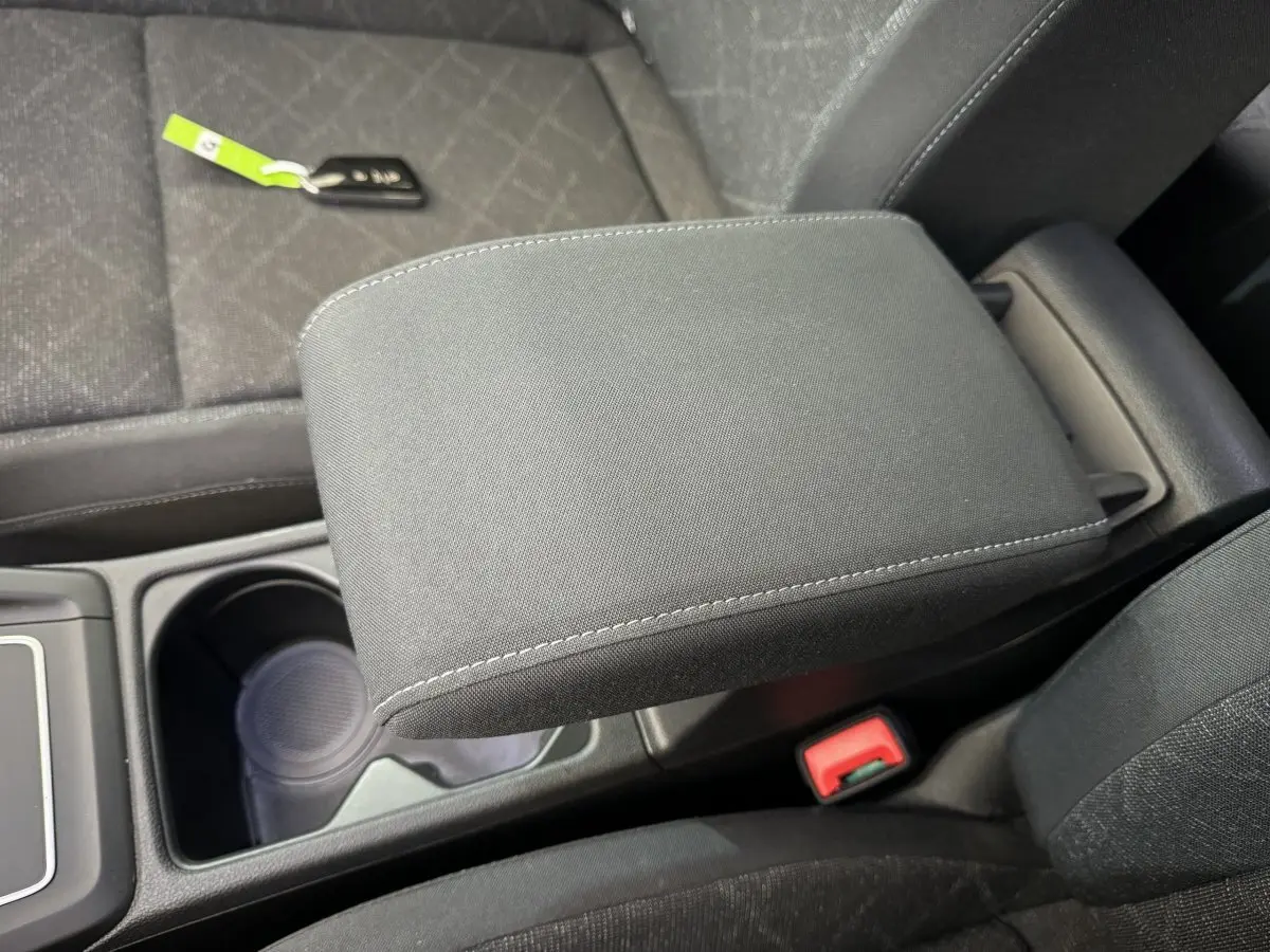 Gros plan sur l'accoudoir central noir et la console entre les sièges avant d'une Volkswagen Golf bleue.