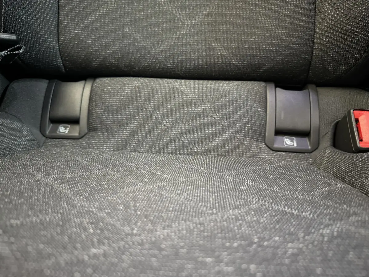 Gros plan sur l’assise arrière en tissu gris foncé avec fixations ISOFIX et boucle de ceinture rouge visible.