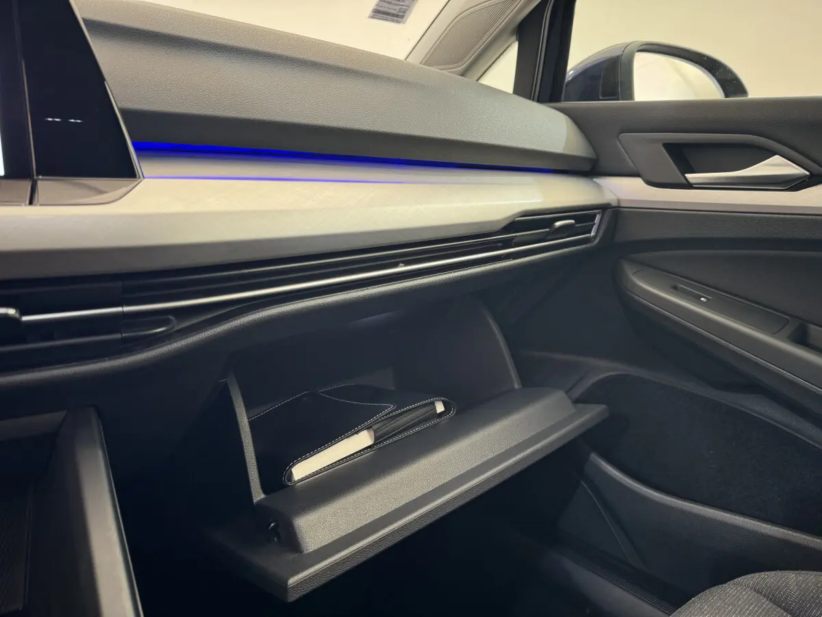 Intérieur côté passager de la Volkswagen Golf 2.0 TDI bleu, tableau de bord avec éclairage bleu et boîte à gants ouverte.