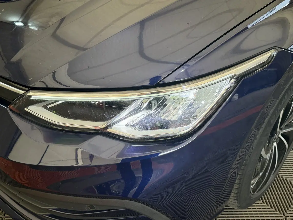 Gros plan sur le phare avant droit d'une Volkswagen Golf bleu foncé, avec une jante noire visible en arrière-plan.