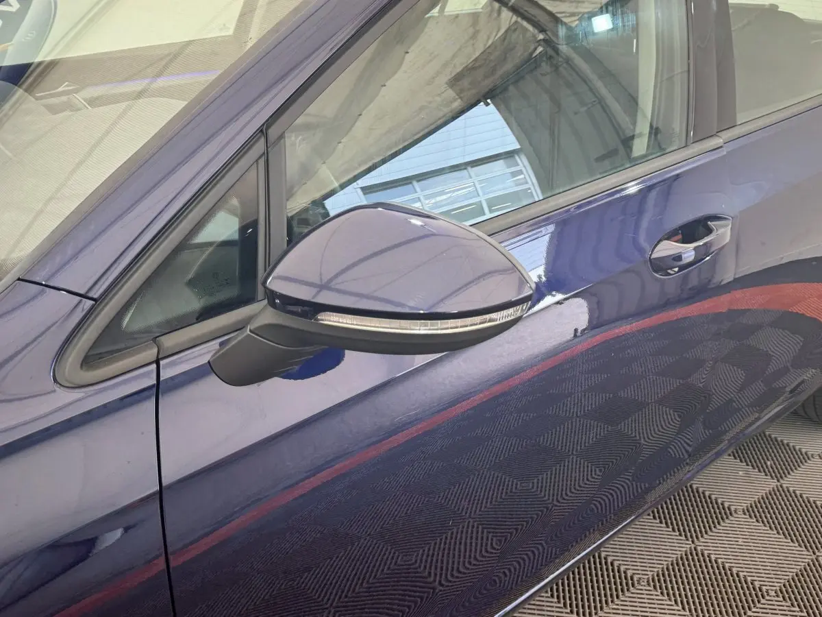 Vue rapprochée du rétroviseur côté gauche d'une Volkswagen Golf bleu métallisé 2021 avec poignée de porte visible.