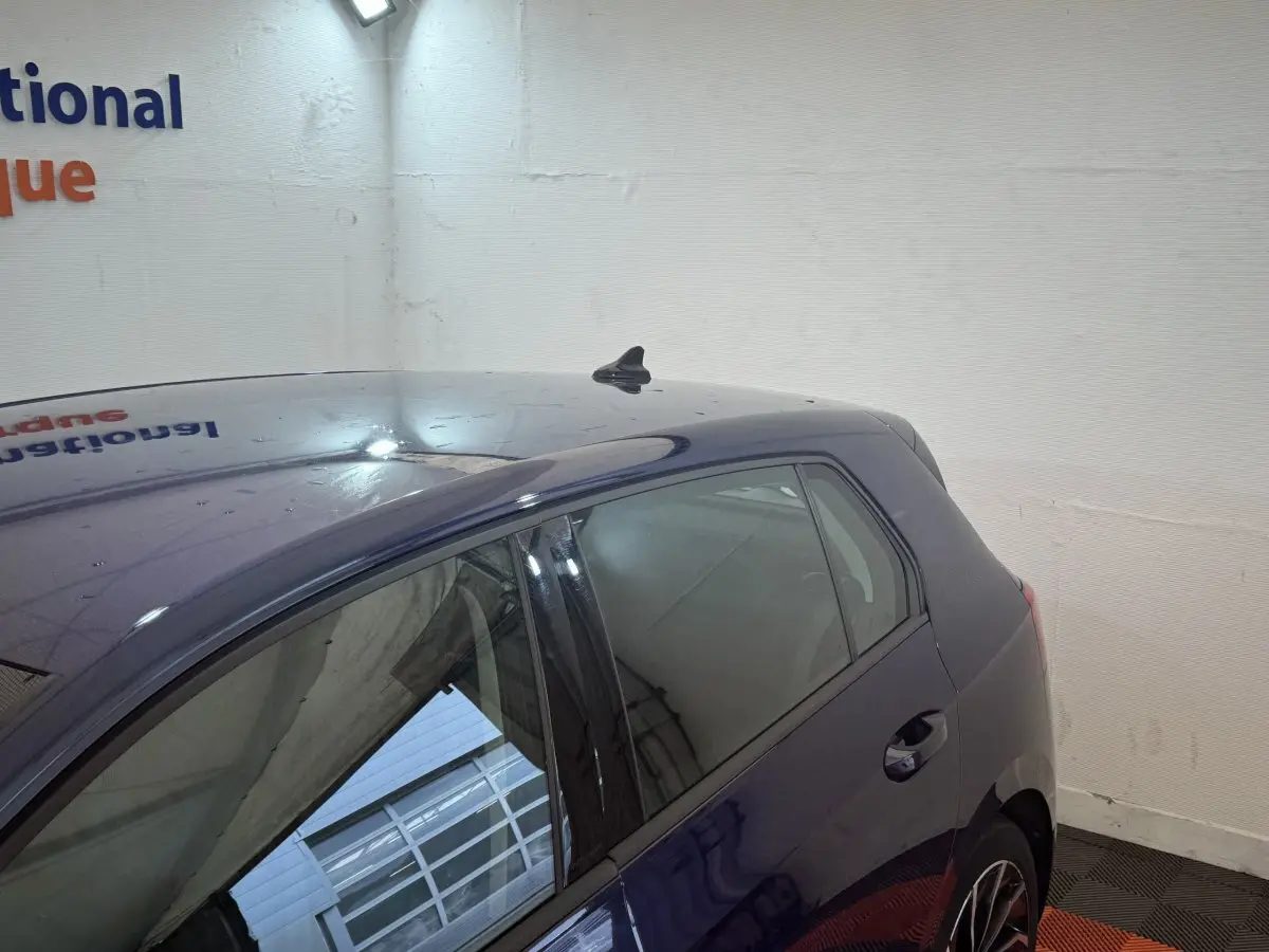 Vue 3/4 arrière droite d'une Volkswagen Golf bleu métallisé garée en intérieur, avec antenne requin sur le toit.
